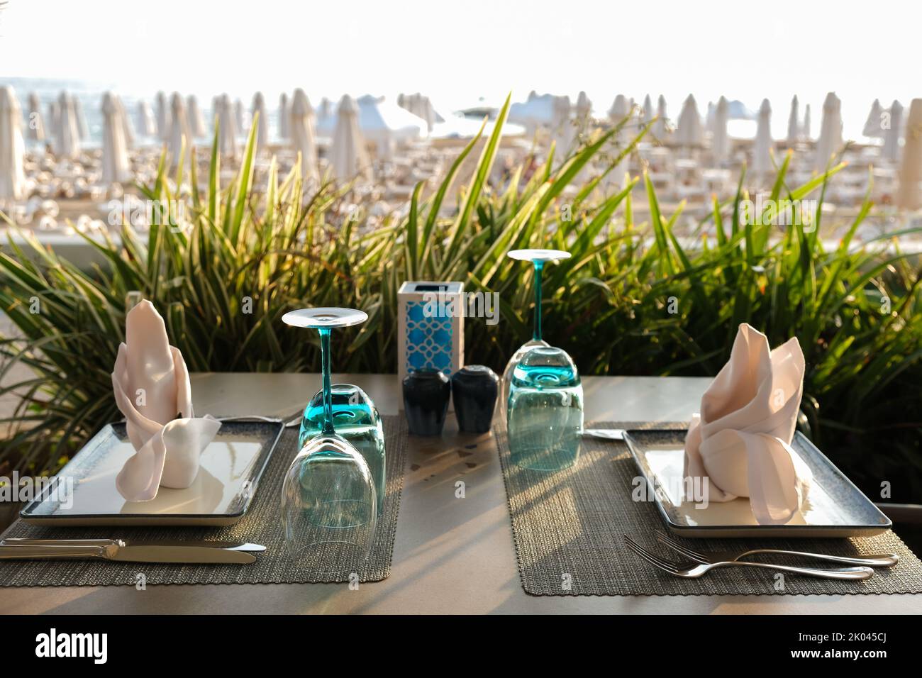 Empty plates and glasses, fabric napkins on the dining table overlooking the sea and the beach in the resort restaurant. Copy Space. Stock Photo
