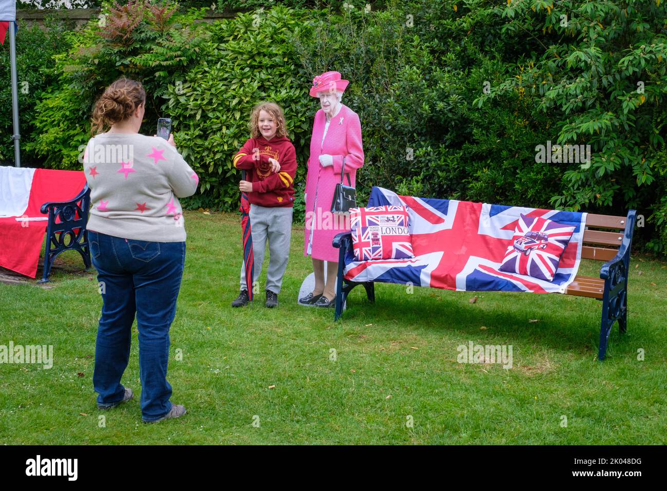 A mother photographs her young daughter beside a lifesize cardboard cut-out of Her Majesty Queen Elizabeth II at a Platinum Jubilee party Stock Photo