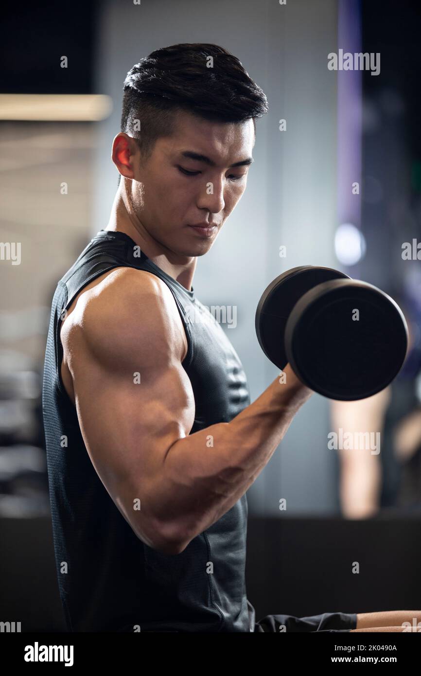 Young Chinese man working out with dumbbell at gym Stock Photo