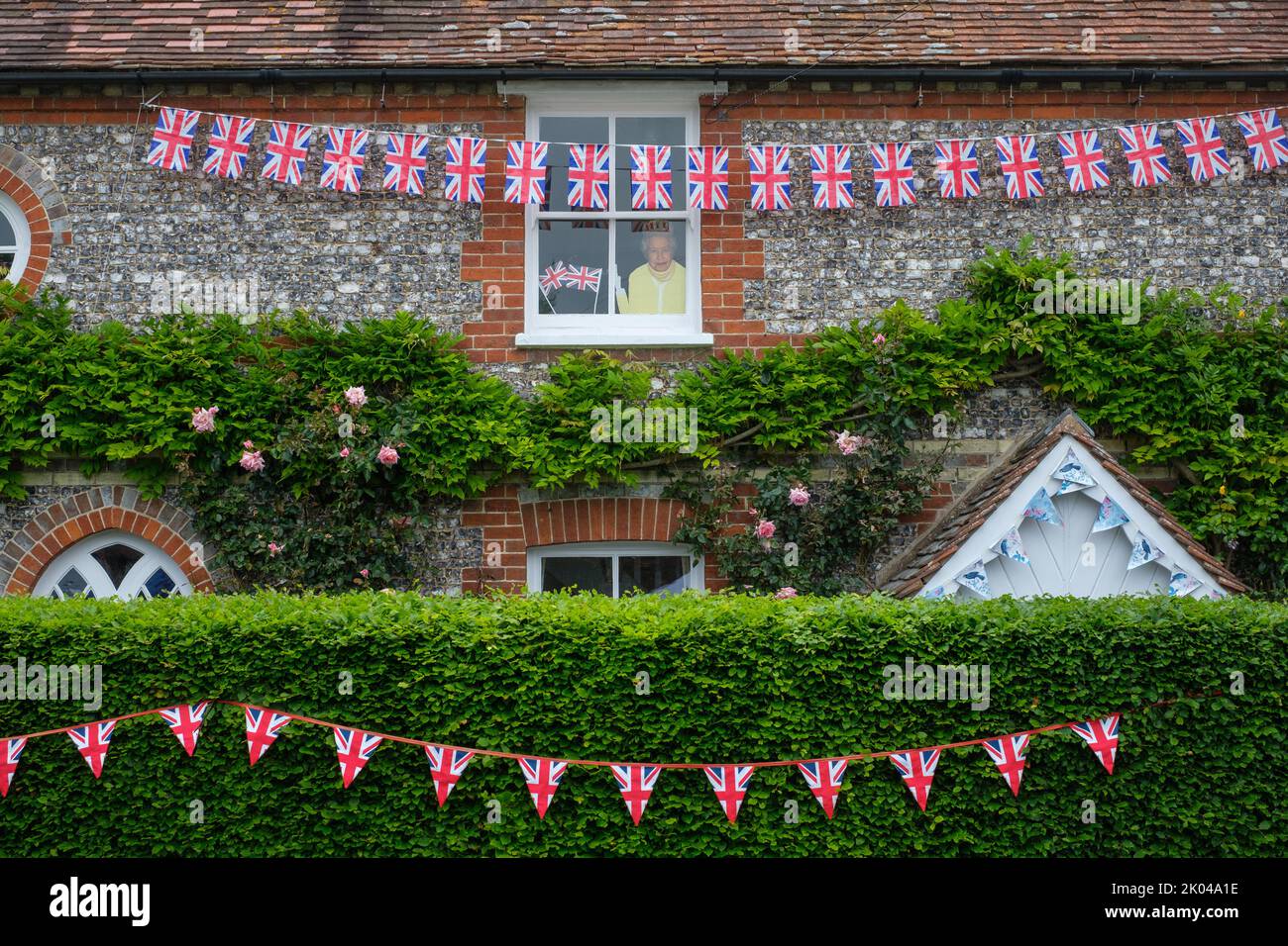 A hand-painted cut-out of Her Majesty Queen Elizabeth II looks down from a window on a Platinum Jubilee street party in the rural village of Turville Stock Photo