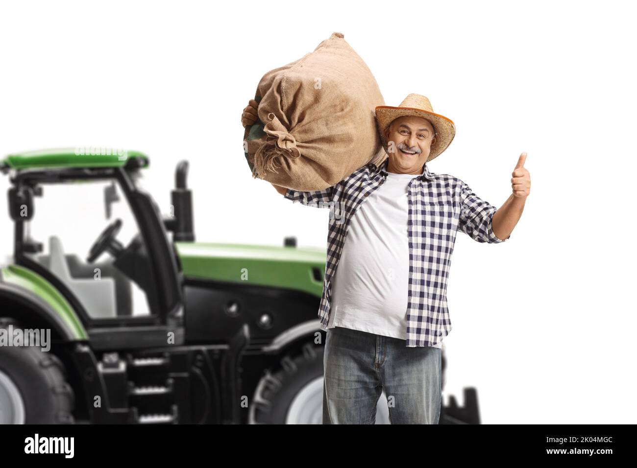 Mature farmer with a sack gesturing thumbs up in front of a tractor isolated on white background Stock Photo
