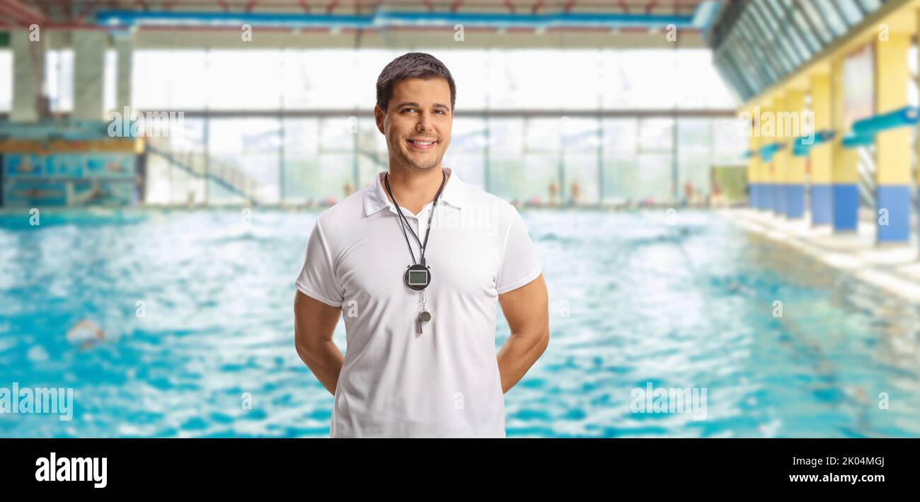 Swimming coach with a wistle and stopwatch posing on an indoor swimming