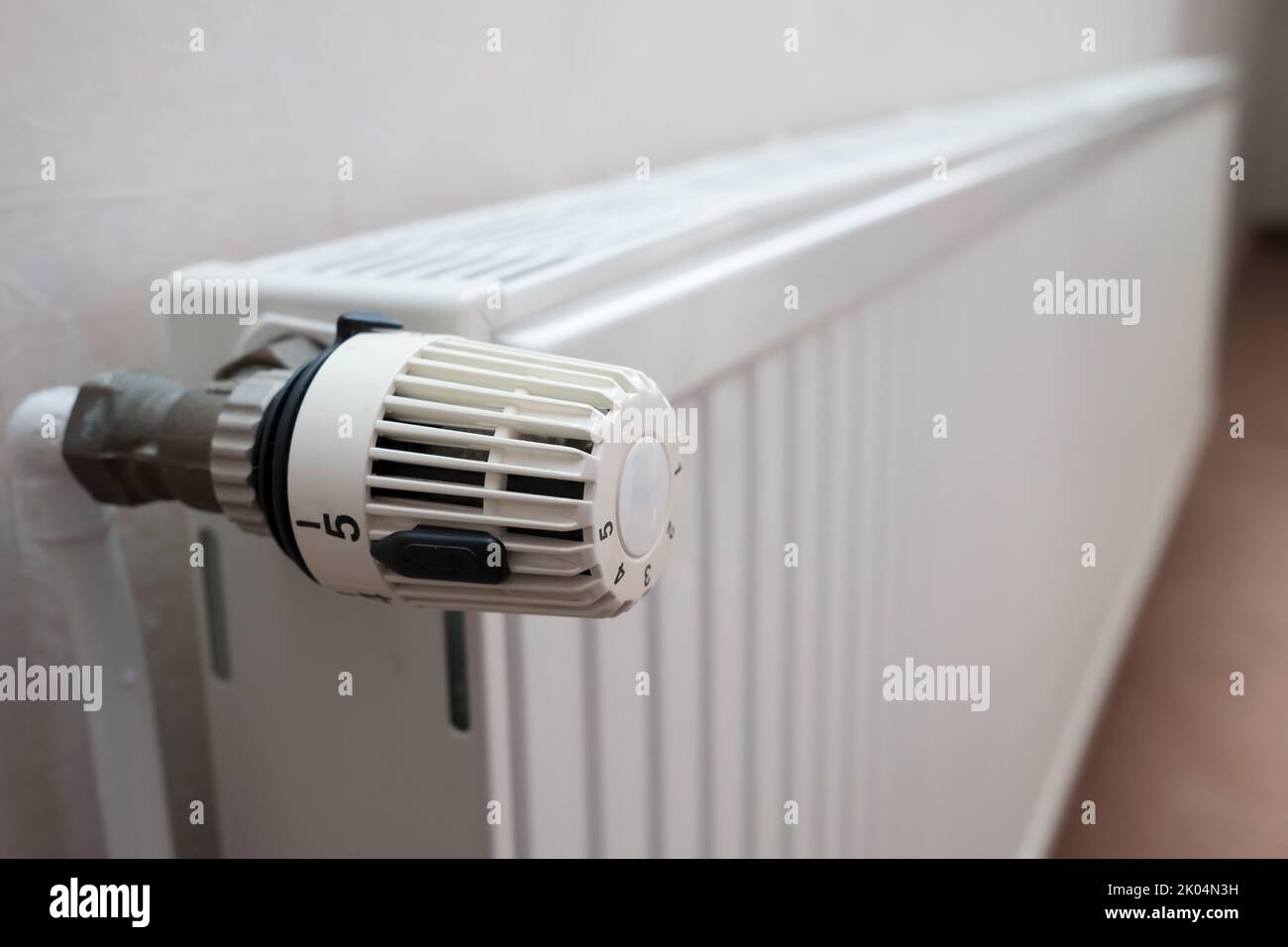 Radiator with thermostat and the ability to turn the knob and reduce the heating temperature. Concept of crisis and increase in heating costs.  Stock Photo