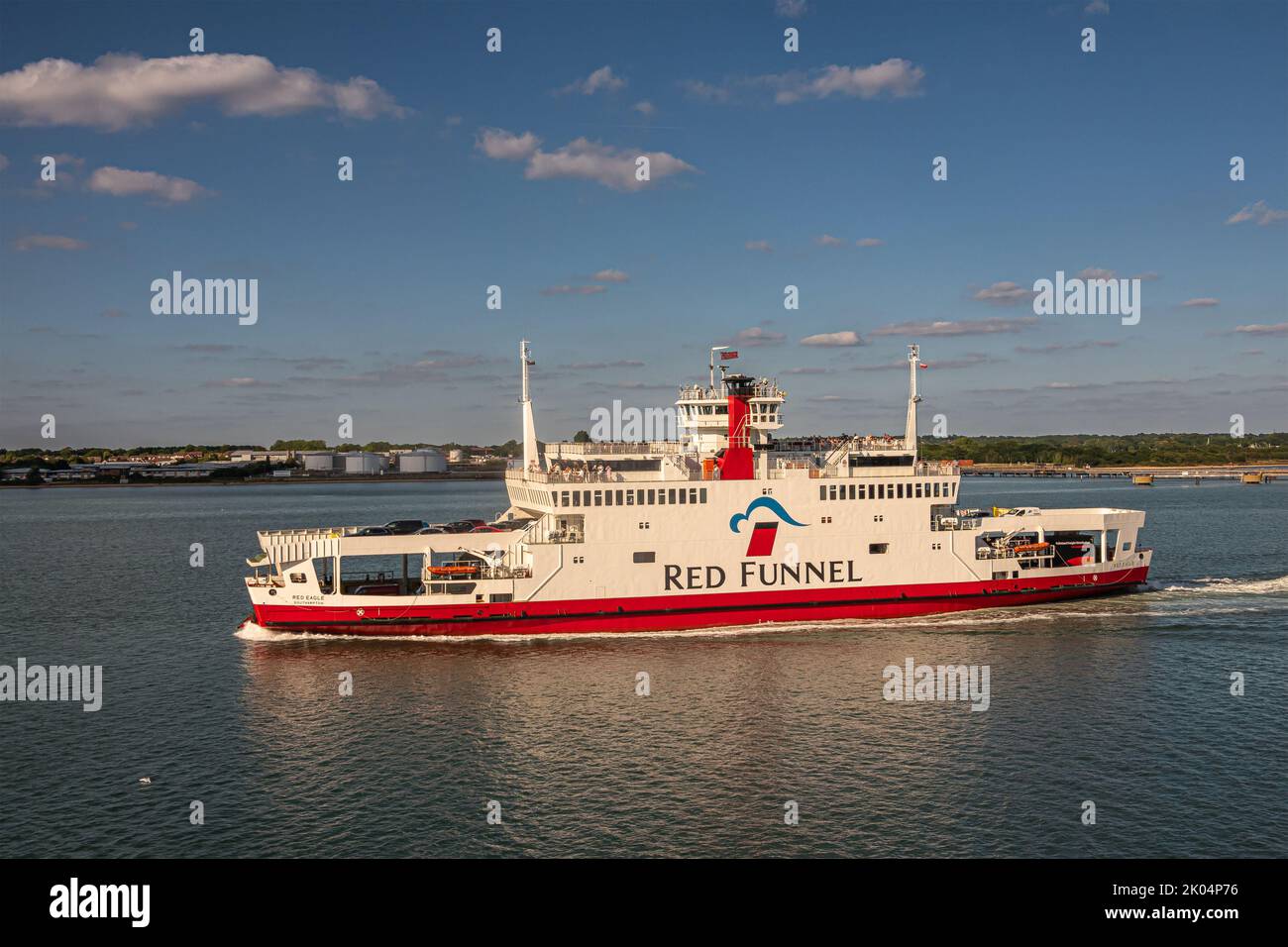 Southampton, England, UK - July 7, 2022: Closeup, Red Funnel ferry traverses East Cowes blue water under blue cloudscape with port installations on ho Stock Photo