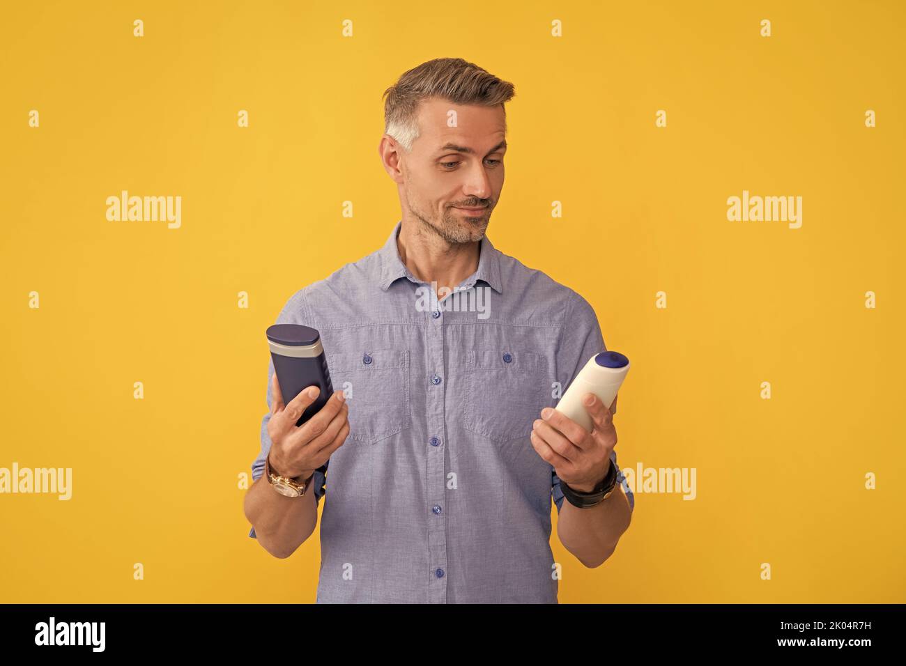 man choose shampoo on yellow background, haircare Stock Photo