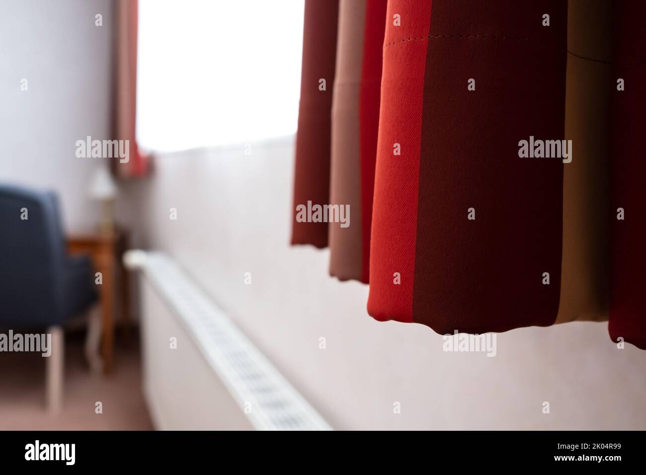 Red curtains hang on the window, in the hotel room, in a cozy interior.  Stock Photo
