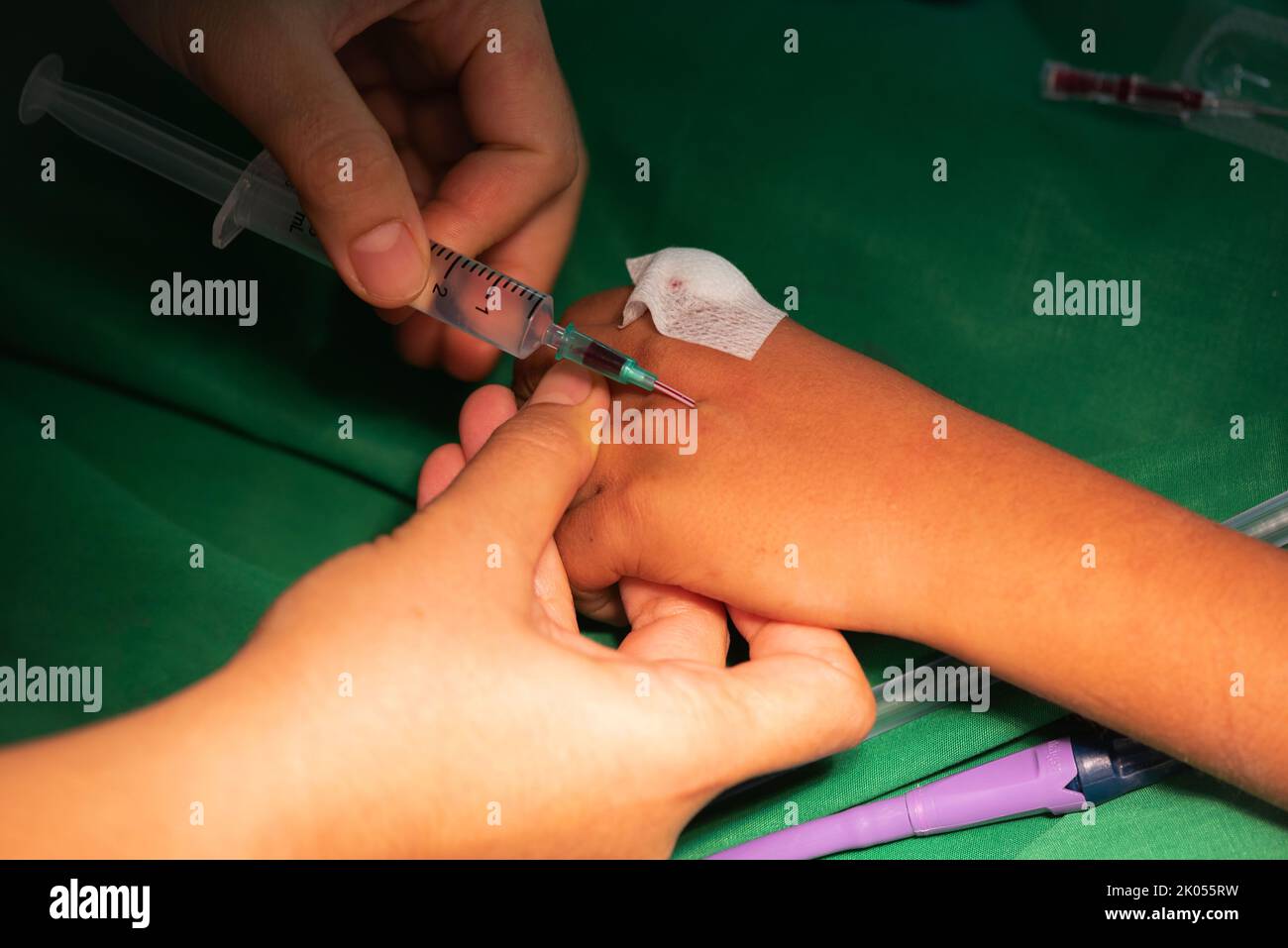 Doctor inserting needle for intravenous fluid  in child hand during surgery. Stock Photo