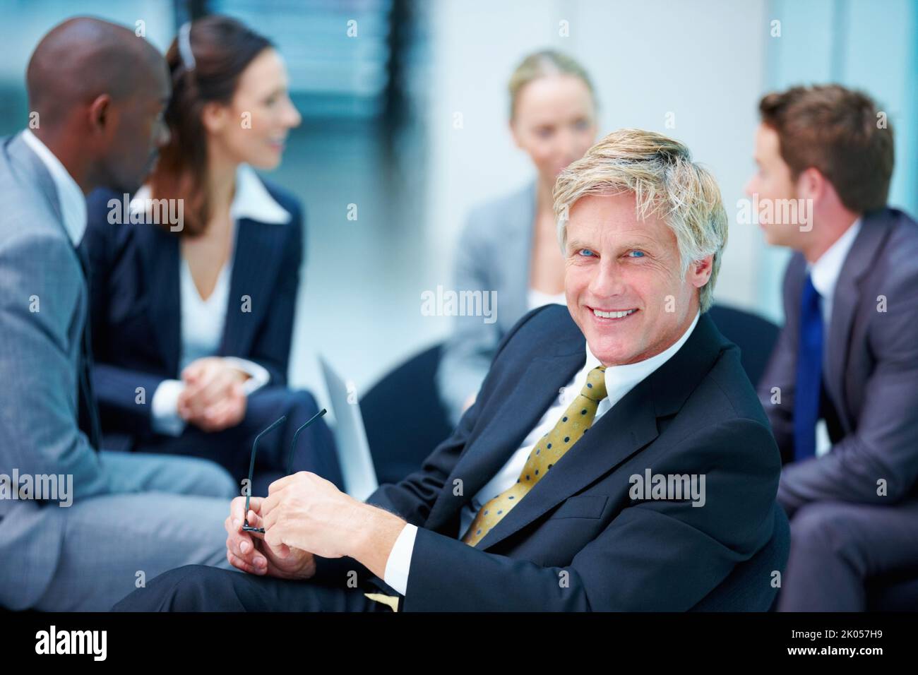 Mature business man smiling with confidence. Portrait of confident mature business man smiling while holding glasses with executives in background. Stock Photo