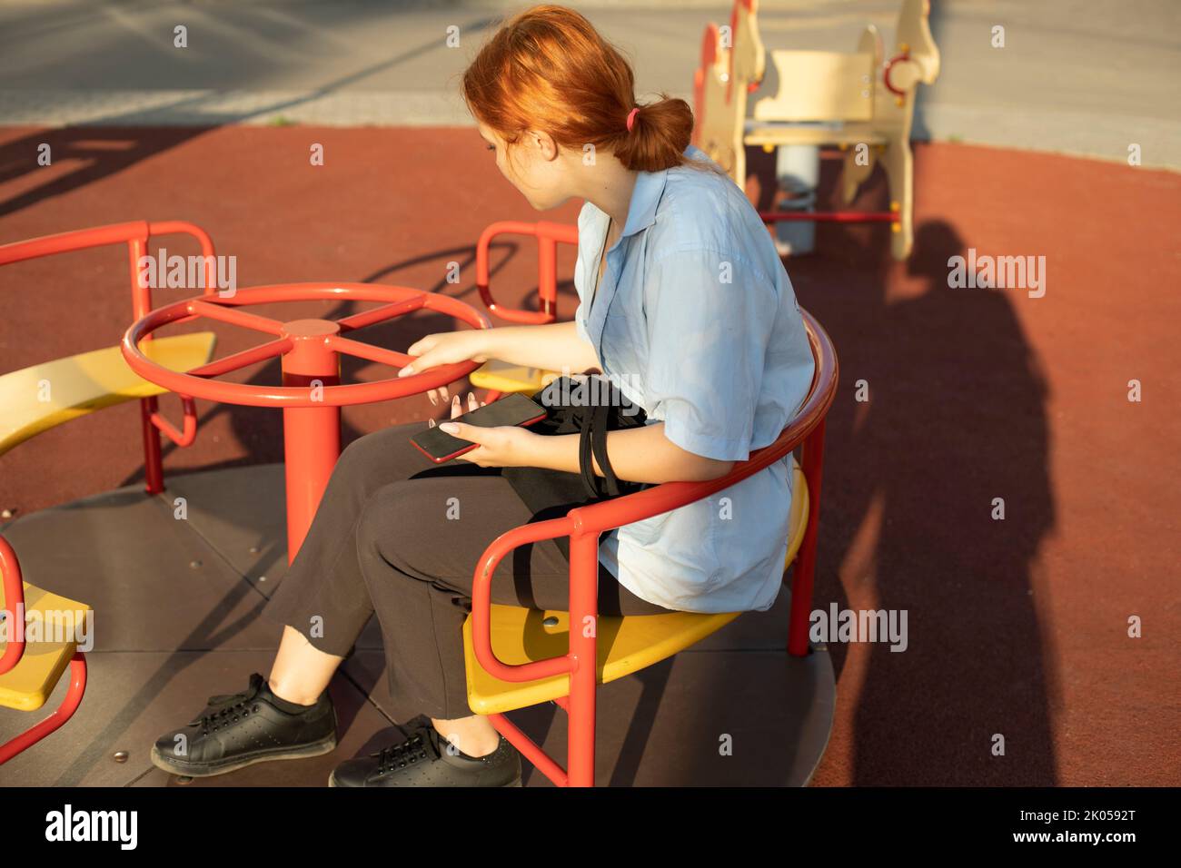 Girl sits on playground. Schoolgirl on carousel. Teenager in summer. Student waits on swing . Stock Photo