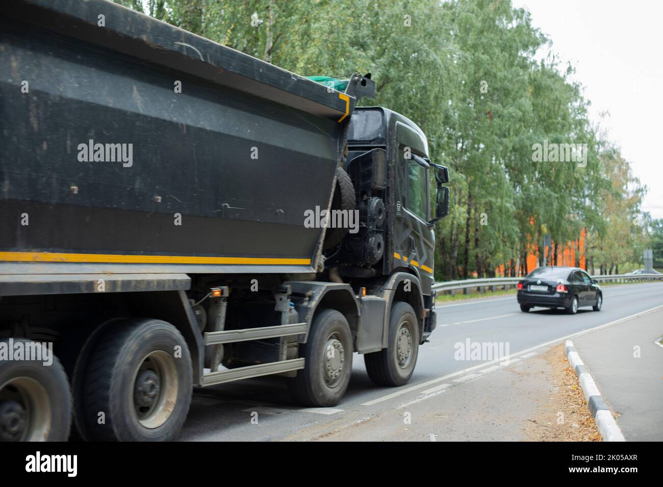 Black truck on road. Freight transport on highway. Car with body. Great trailer. Transportation of sand. Stock Photo