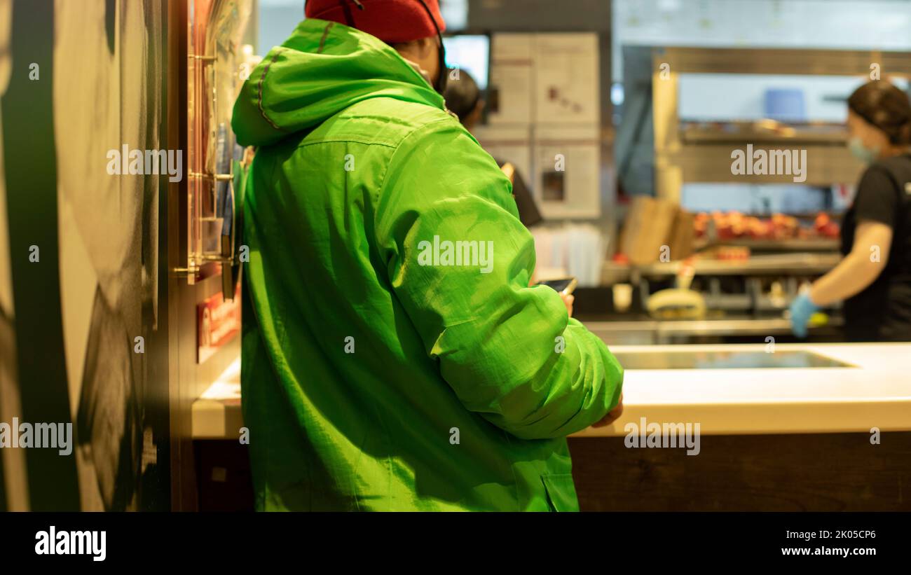 Courier picks up food at restaurant. Green jacket on courier. Food delivery man. Stock Photo