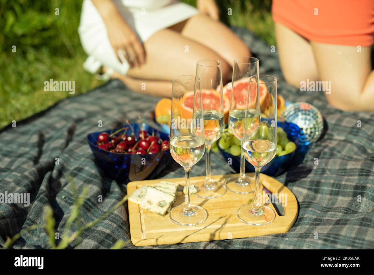 Picnic in summer in park. Food on background of girls. Champagne glasses. Details of rest in park. Food on street. Fruits mime drinks. Stock Photo