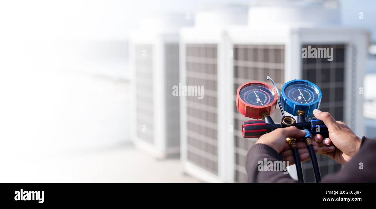 Air repair mechanic using measuring equipment for filling industrial factory air conditioners and checking maintenance outdoor air compressor unit. Stock Photo