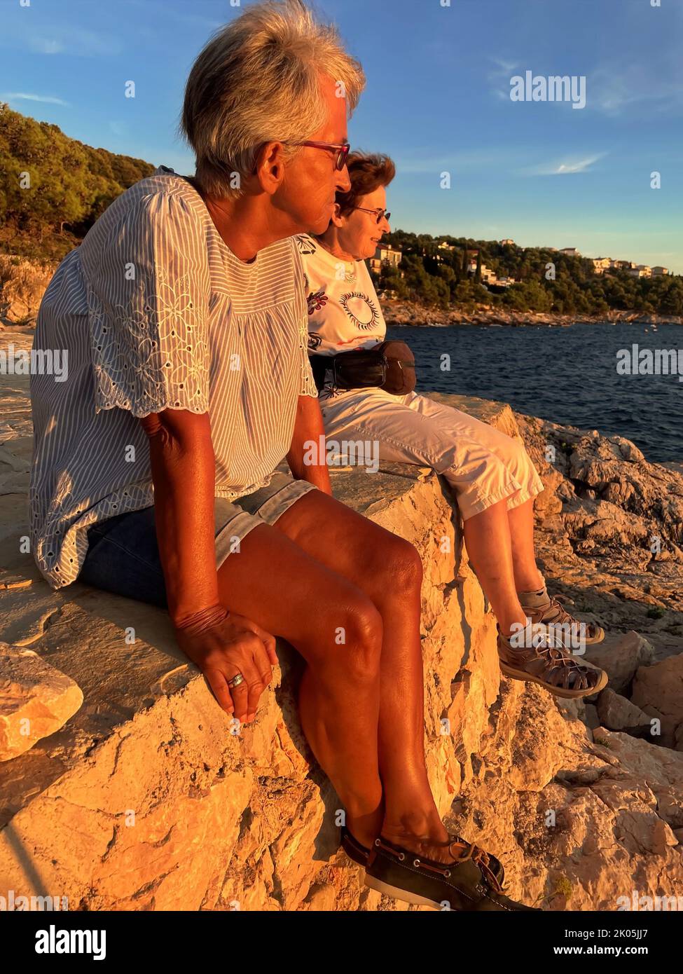 Two senior women sitting on the sea shore Stock Photo