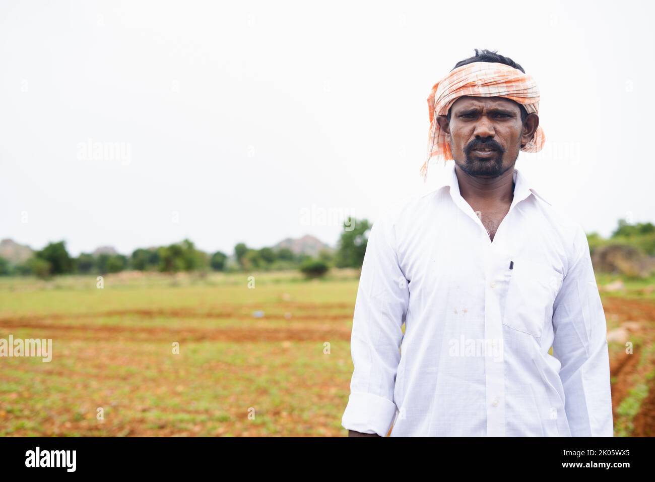 Portrait shot of Indian farmer standing by looking camera at farmland with copy space - concept of agriculture and rural India. Stock Photo