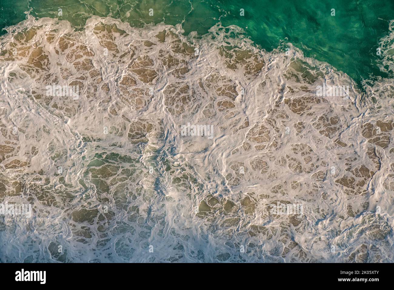 Top view of patterns of white foam from the impact of ocean waves on coastal rocks. South Africa Stock Photo