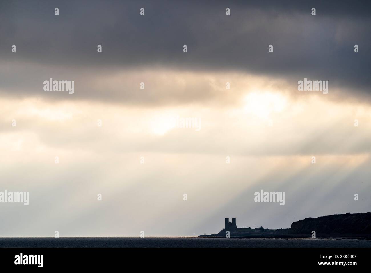 Storm clouds over the sea and coast at Reculver with the twin towers of the ruined 12th century church silhouetted against the sky. Strong sunbeams pouring through the thick cloud layer to the sea. Stock Photo