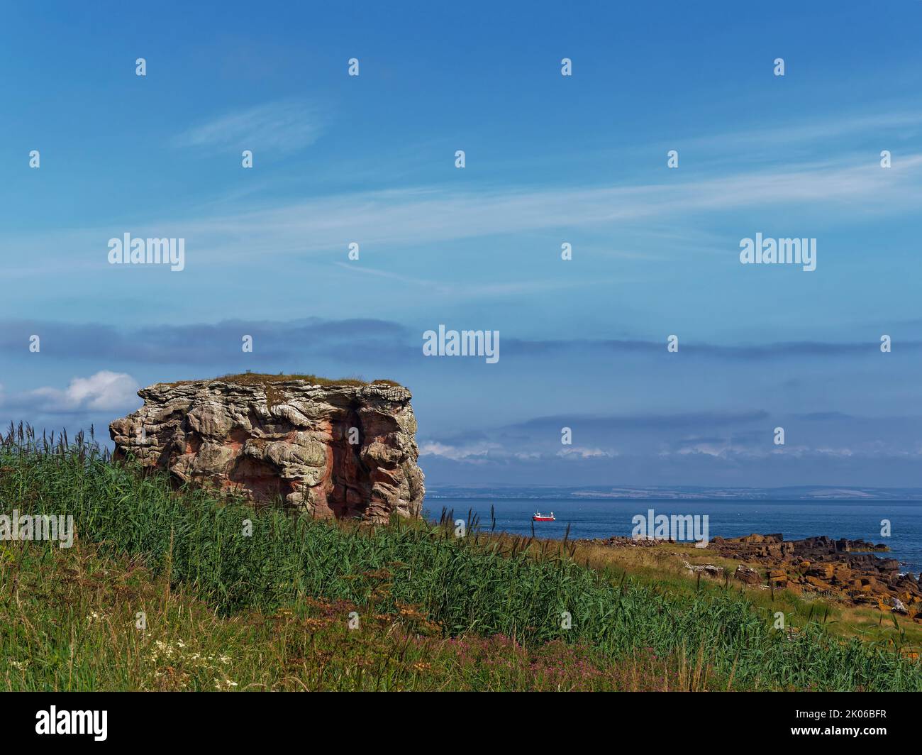 A Fishing Boat behind Buddo Rock in St Andrews Bay seen from the Fife Coastal Path on a calm Summers Morning in July. Stock Photo