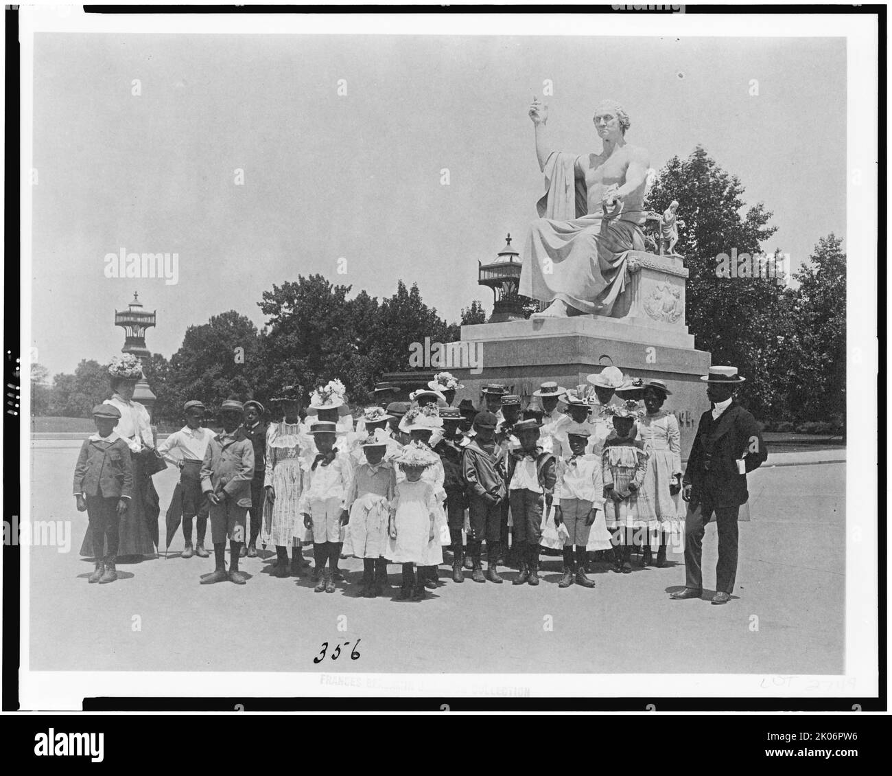 Group of school children in front of statue of George Washington, Washington, D.C., (1899?). [African American children on a school trip, with the 'Enthroned Washington' sculpture by Horatio Greenough behind. George Washington is depicted as a Roman emperor in a toga]. Stock Photo