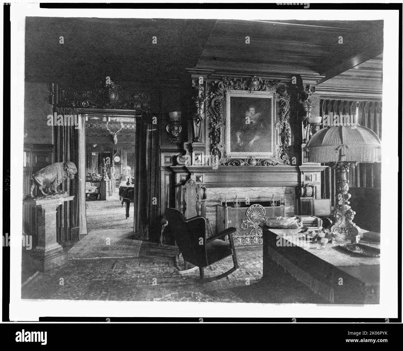 Study with portrait of woman in Elizabethan dress, over fireplace, fringe lamp at right, and buffalo statue on left; elk head on wall and grandfather clock in background, in home of Edmund Cogswell Converse, Greenwich, Connecticut, 1908. The Conyers Farm estate, designed by Donn Barber c1904, was owned by businessman Edmund C. Converse. Stock Photo
