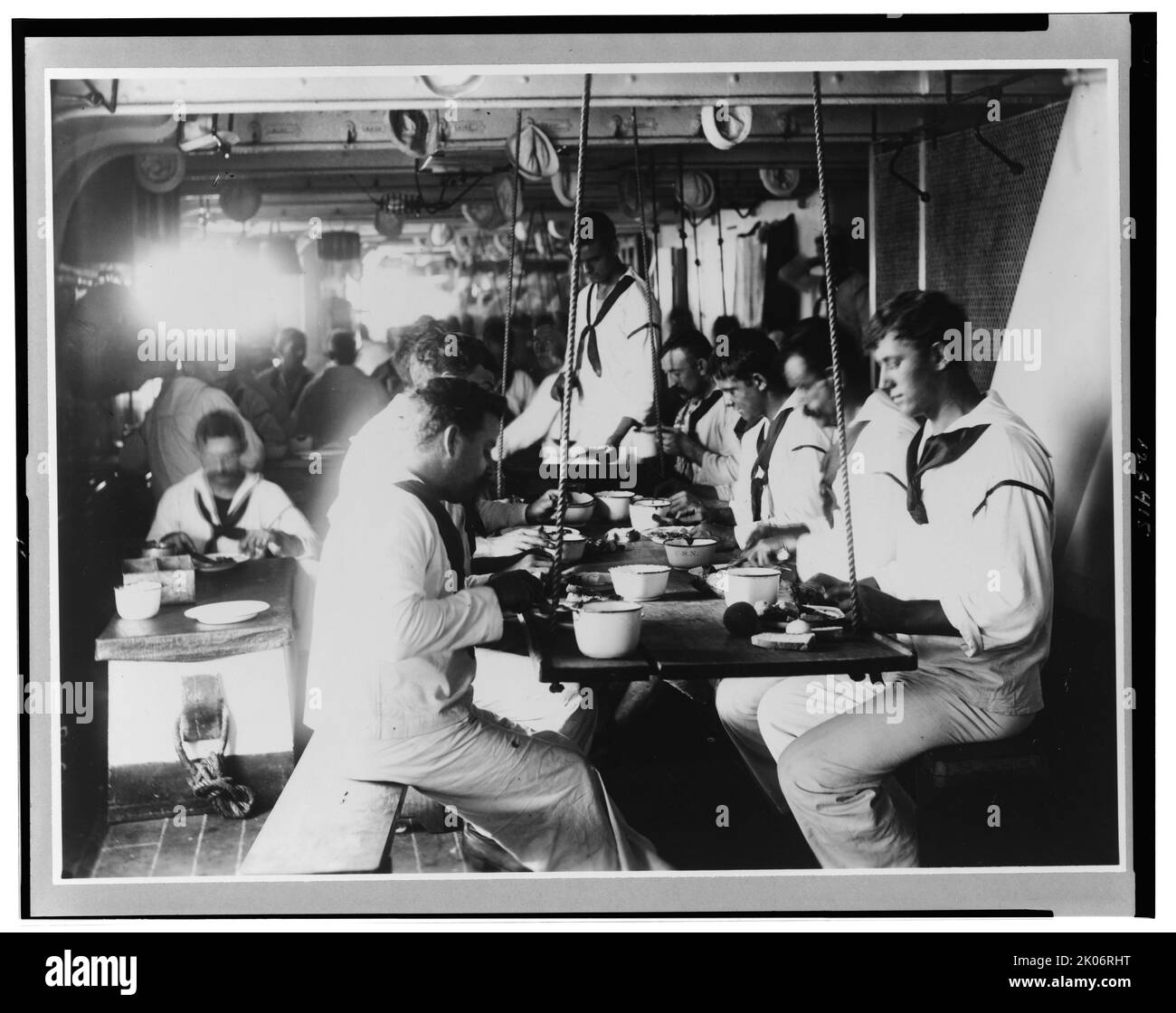 U.S.S. Olympia - crew's mess, 1899. Interior view of dining area aboard the USS Olympia, showing sailors eating at a table suspended by ropes. Stock Photo