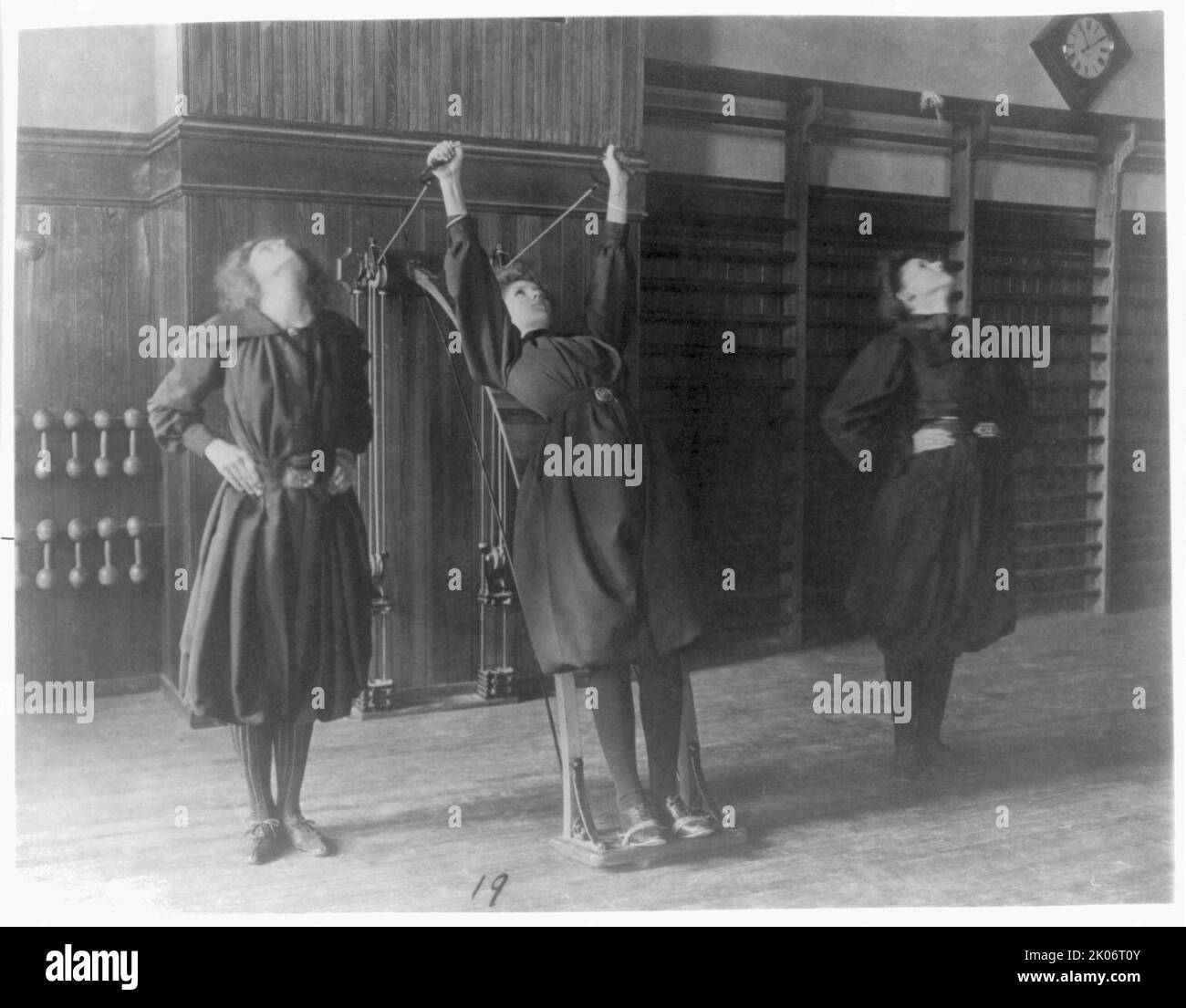 Female students exercising, one with a wall-mounted device using ropes ...
