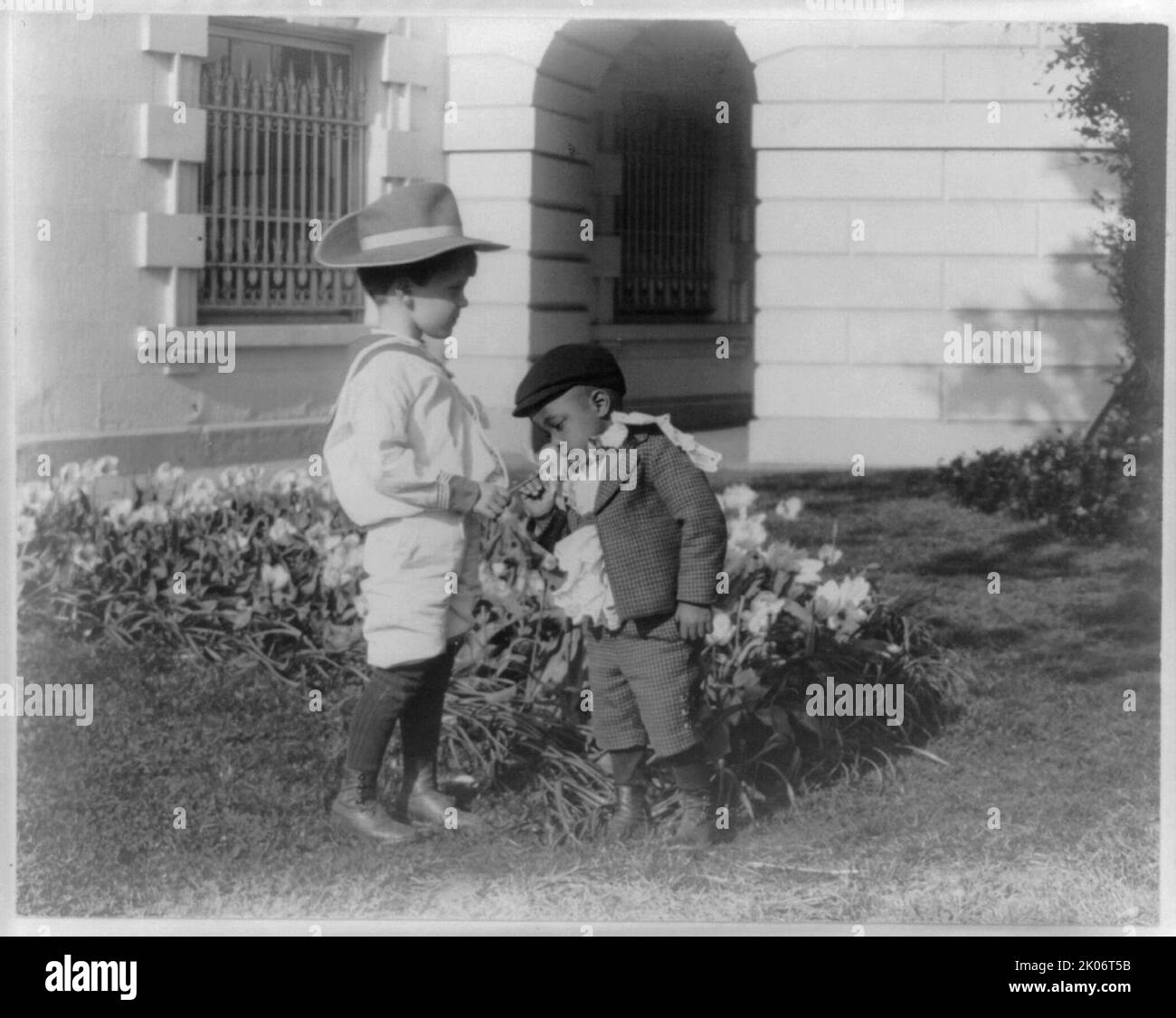 Quentin Roosevelt as a child in front of a flower garden and Roswell Newcomb Pinckney smelling a flower at the White House, Washington, D.C., between 1900 and 1905. Stock Photo