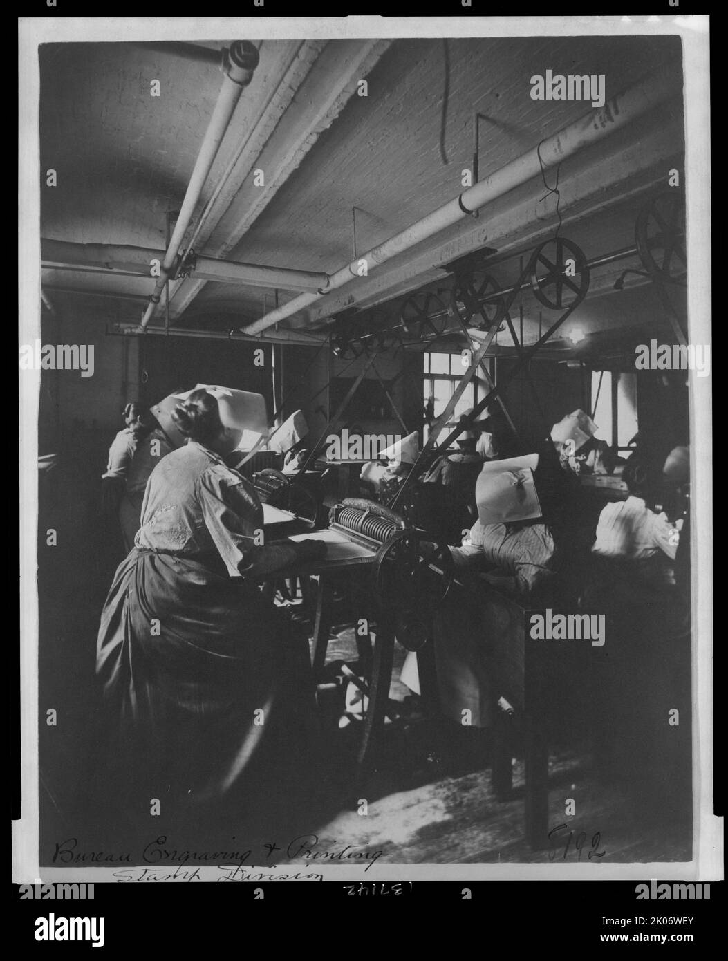 Women perforating sheets of stamps in the Stamp Division at the Bureau of Engraving &amp; Printing, c1895. Photograph shows a group of women perforating stamps. Power is provided by steam driven belts. The women wear paper hats to protect them from airborn dust. Stock Photo