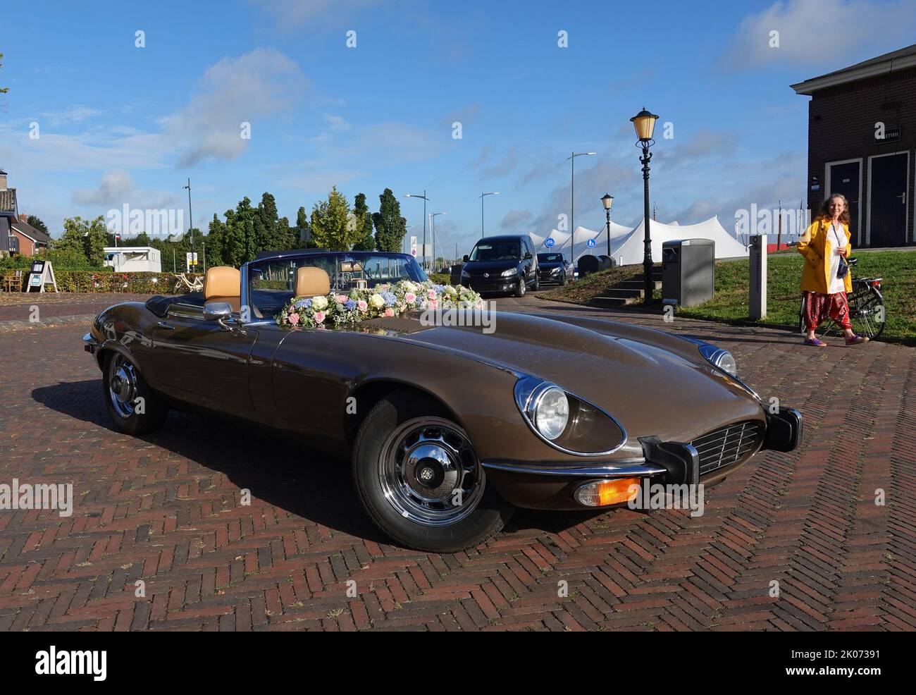 Elburg, Netherlands - Sept 9 2022 A very special rental car for weddings: a cabriolet Jaguar e-type. A woman and lamppost in the background Stock Photo