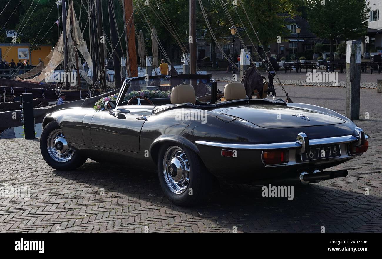 Elburg, Netherlands - Sept 9 2022 A very special rental car for weddings: a cabriolet Jaguar e-type. The old fishing harbor in the background Stock Photo