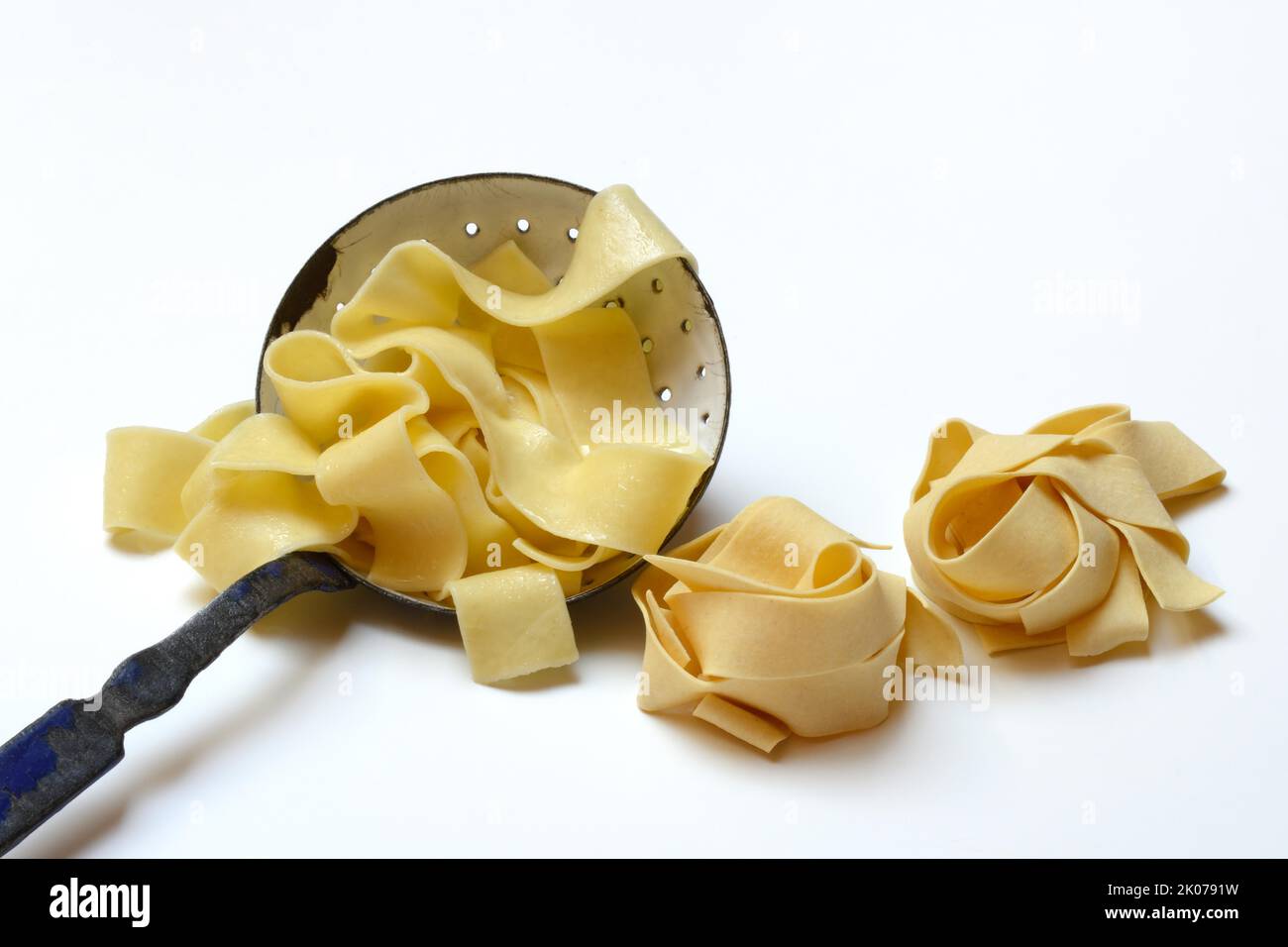 Pappardelle, wide Italian ribbon noodles in strainer ladle and two