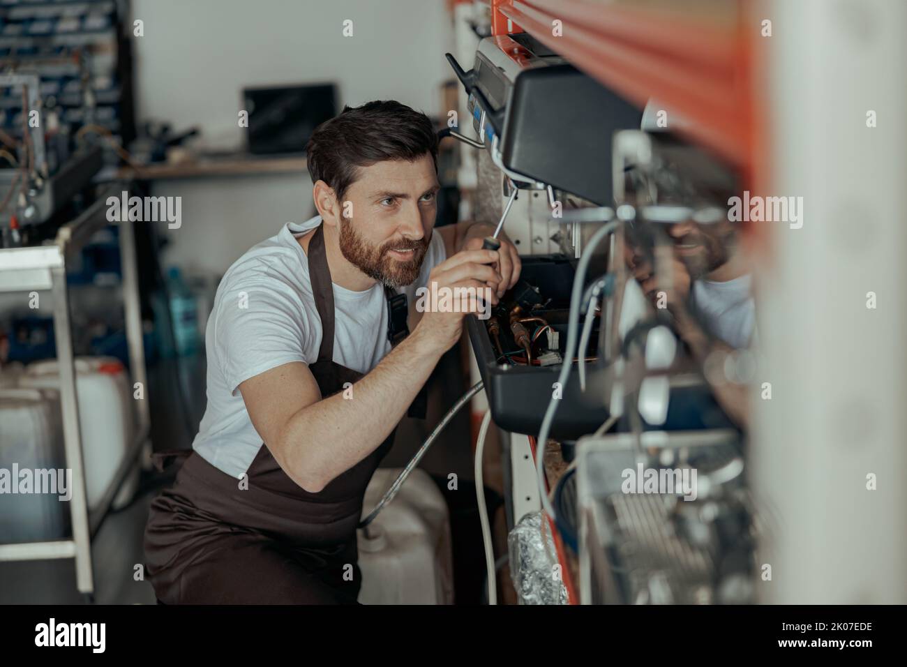Smiling young man repairing coffee machine using screwdriver in a workshop Stock Photo