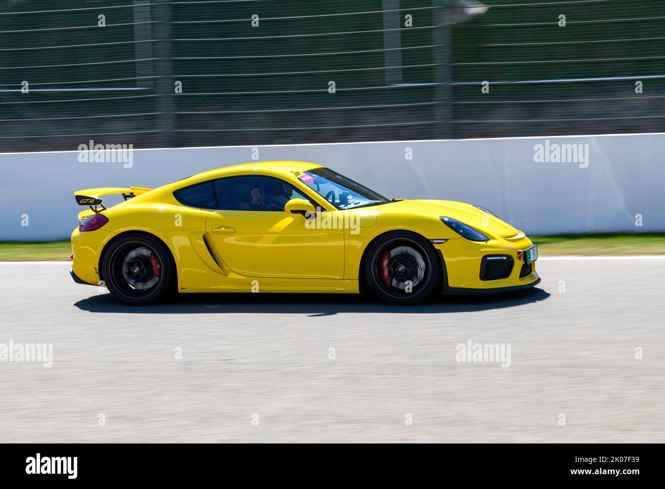 Yellow racing car sports car Porsche Cayman GT4 races at high speed top speed during trackday on start-finish straight of race track, FIA Formula 1 Stock Photo