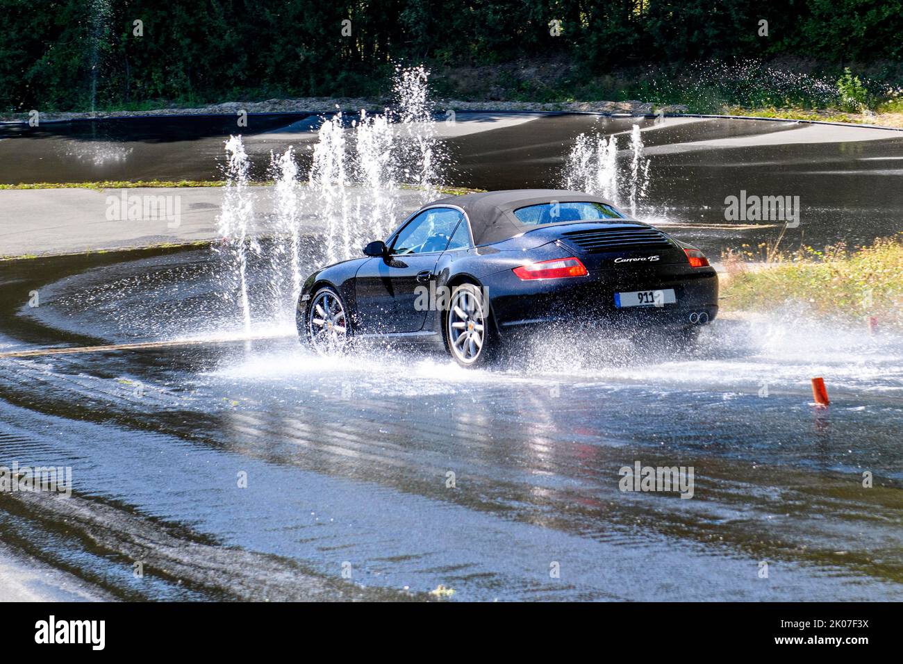Sports car with all-wheel drive Porsche 911 Carrera 4s drives at 50 kmh speed on sloping heavily watered wet road towards obstacle from water Stock Photo