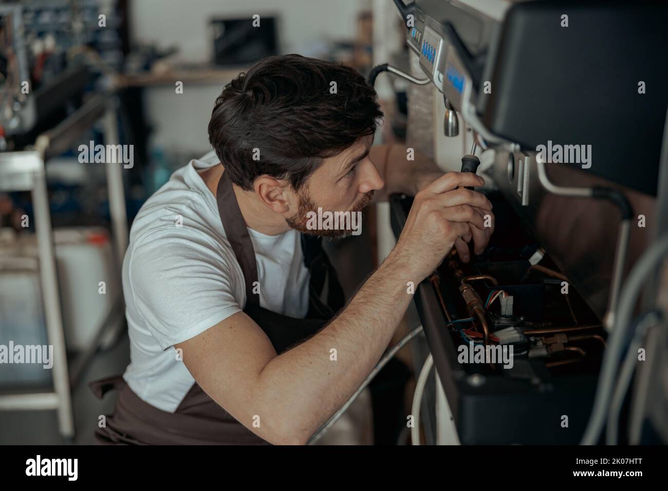Repairman in uniform inspecting coffee machine in own workshop Stock Photo