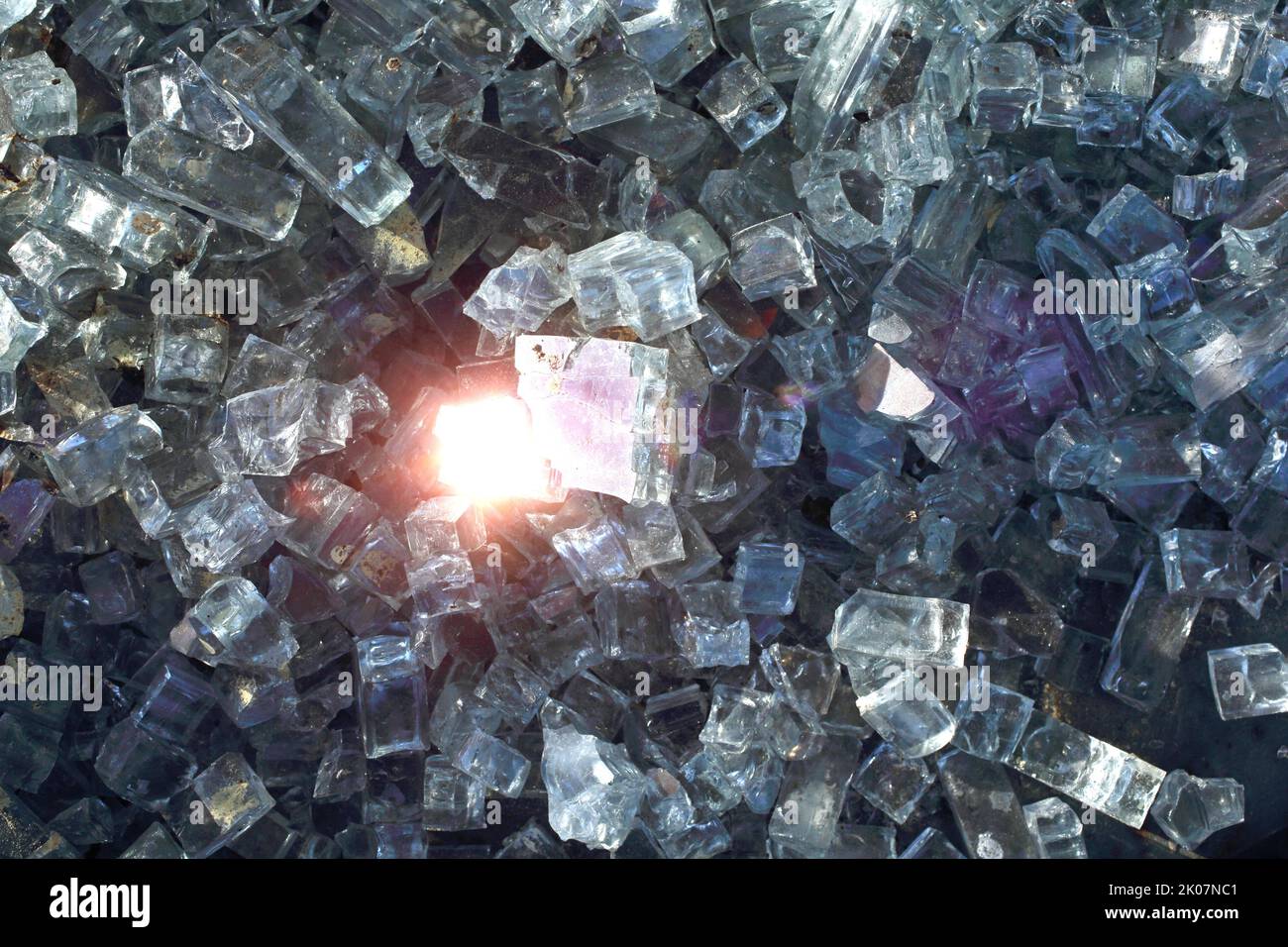 Broken glass pane and a pile of small glass shards and glass splinters with light reflections