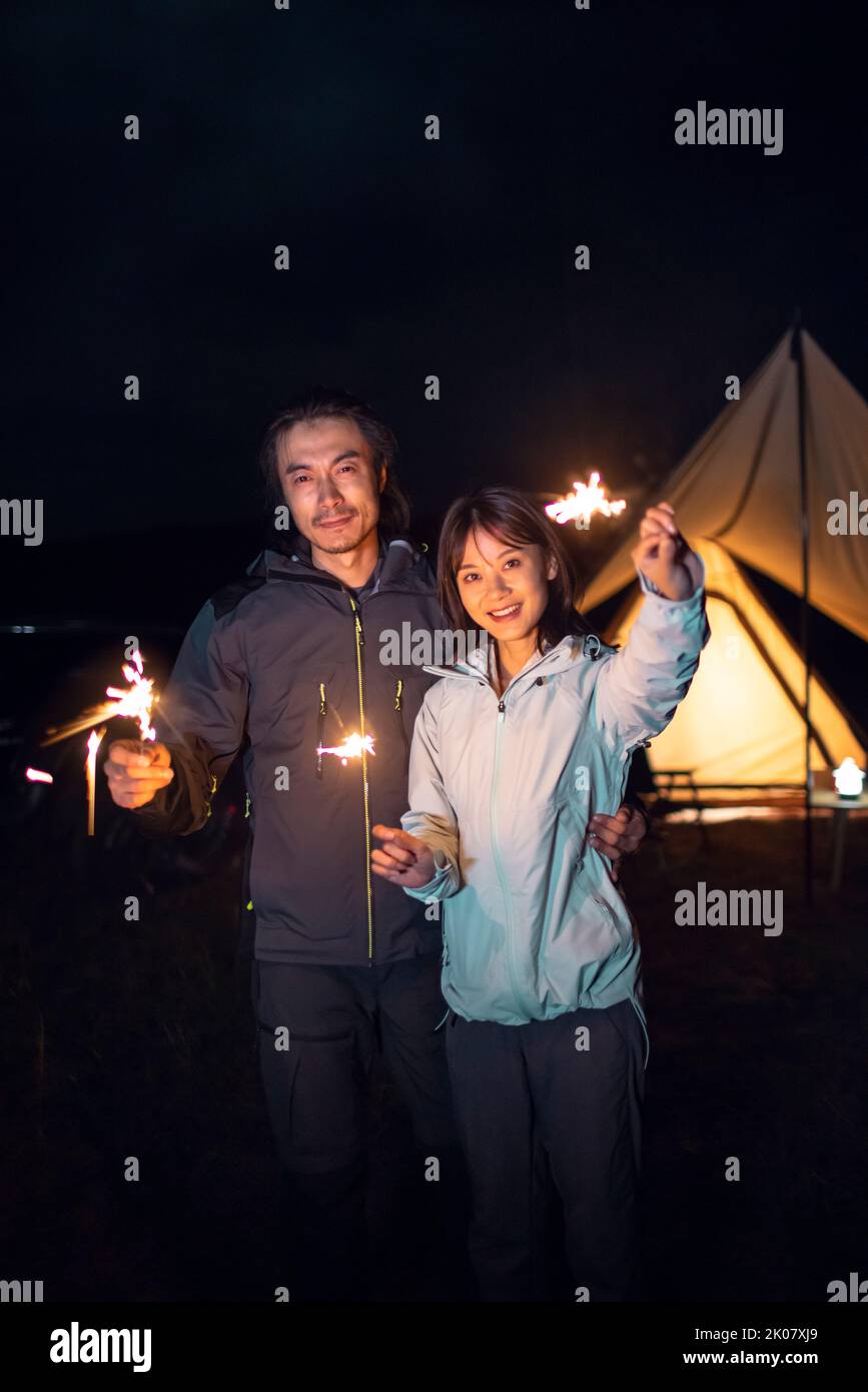 Happy Chinese couple holding sparklers and camping outdoors Stock Photo