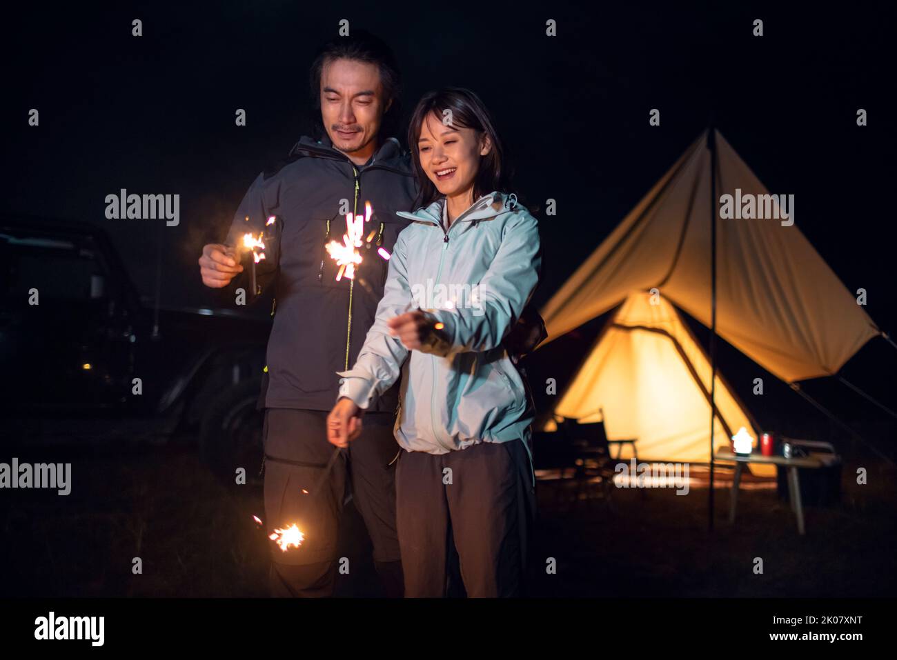 Happy Chinese couple holding sparklers and camping outdoors Stock Photo