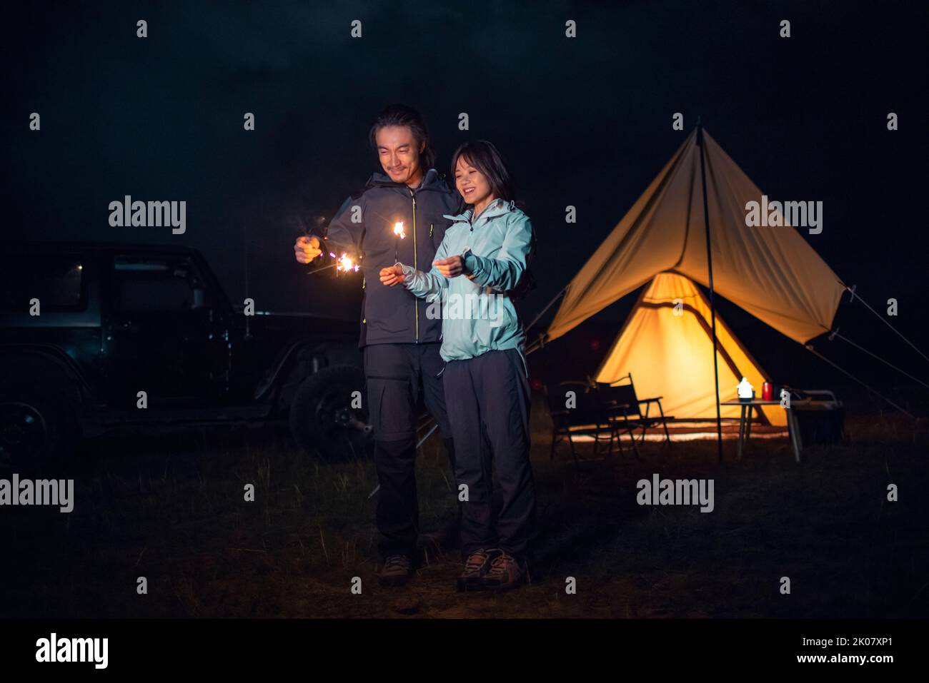 Happy Chinese couple holding sparklers and camping outdoors Stock Photo