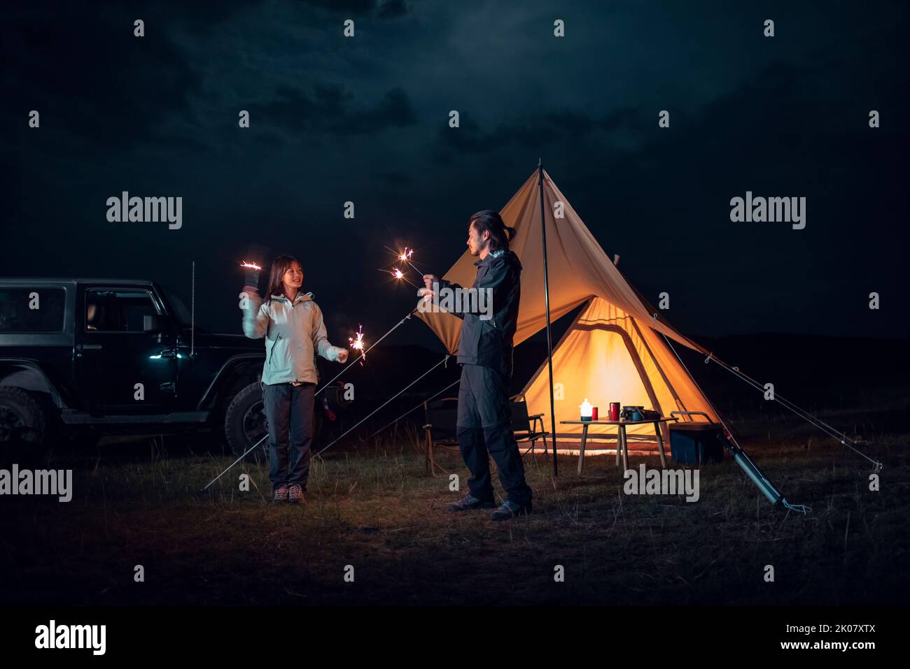 Happy Chinese couple holding sparklers and camping outdoors Stock Photo