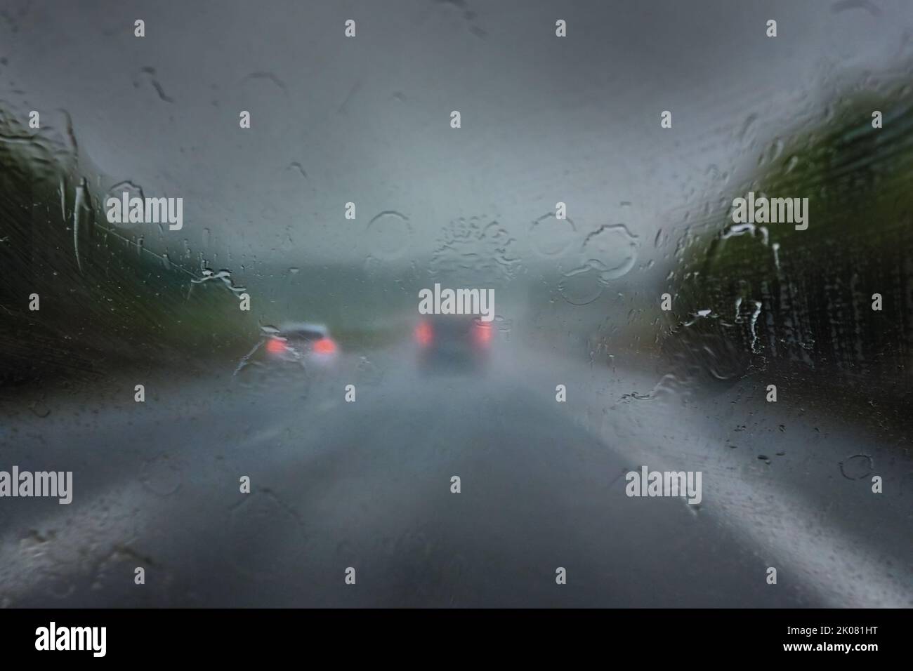 Heavy rain on the highway, thick drops on the windshield and blurred cars with red taillights on the dark road, dangerous weather while driving, traff Stock Photo