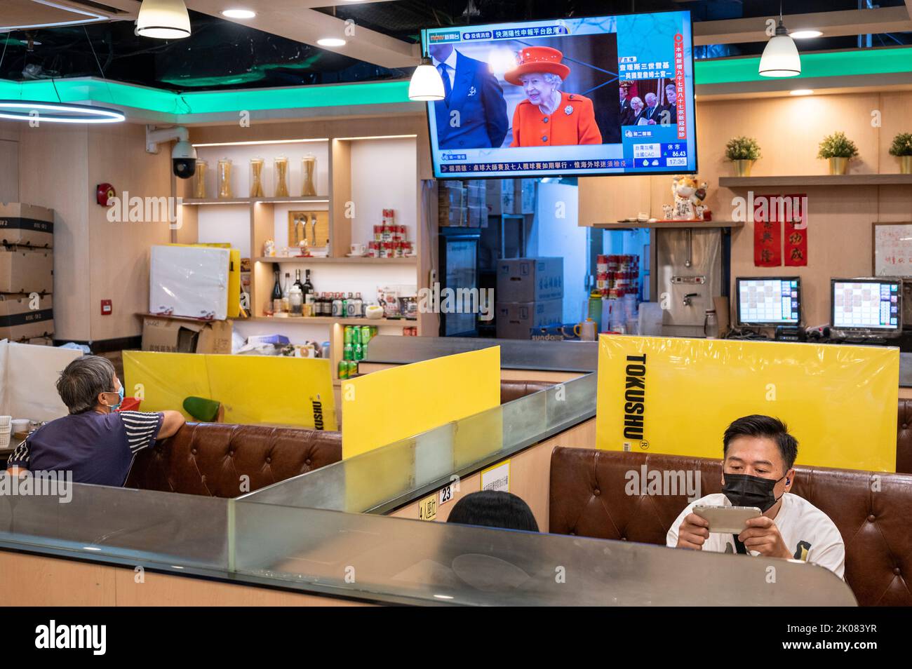 At a local restaurant in the former British colony of Hong Kong, customers eat lunch, a TV news channel shows an image of the longest-serving monarch Queen Elizabeth II a day after her death. Stock Photo