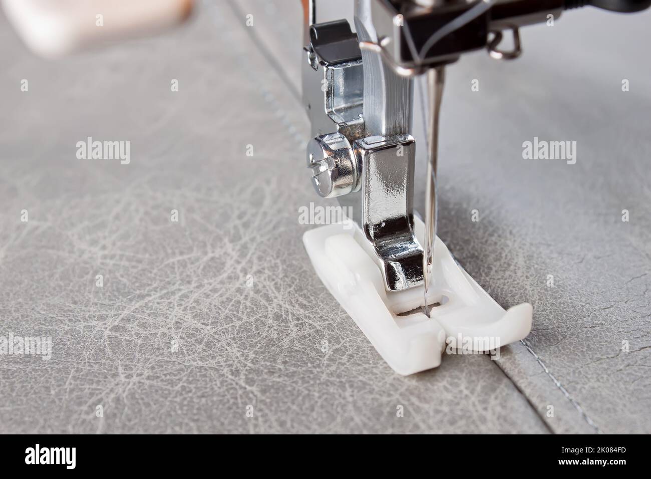 Modern sewing machine with special presser foot makes a seam on grey ...