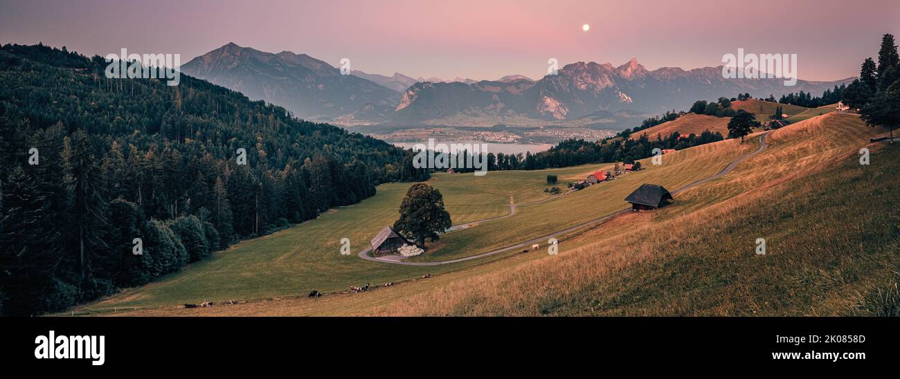A wide panoramic image from a beautiful summer morning during sunrise and the full moon slowly descending behind the mountains. The climatic health re Stock Photo