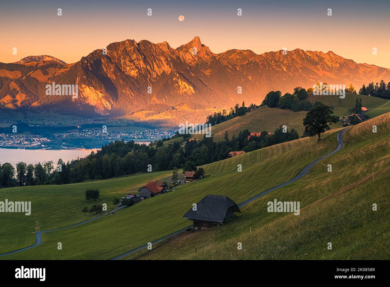 A beautiful summer morning during sunrise and the moon slowly descending behind the mountains. The climatic health resort of Heiligenschwendi is situa Stock Photo
