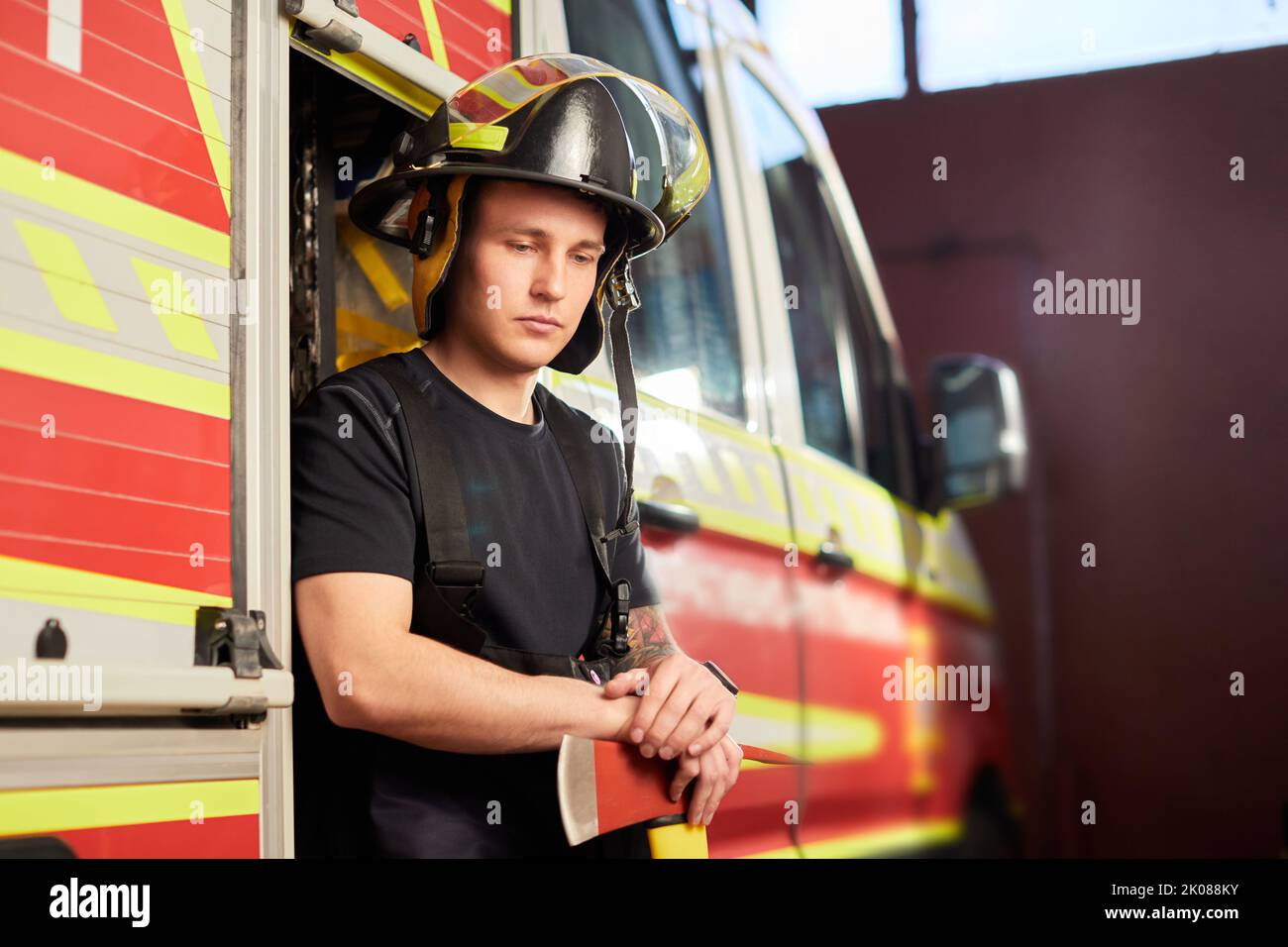 Photo of fireman wearing helmet with ax against fire engine Stock Photo