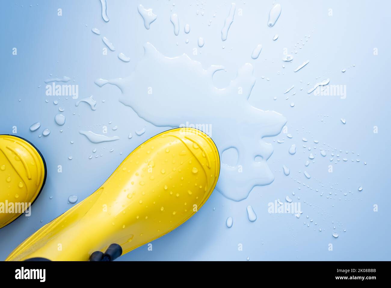 Rubber boots of yellow color stand in a puddle of water on a blue background. Copy space. Flat lay. Top view.  Stock Photo