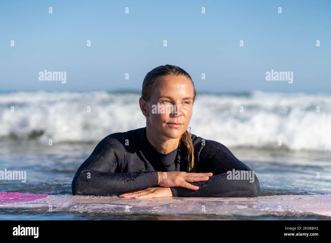 Surfer girl in the water looking at the waves with her surfboard. Female surfer woman Stock Photo