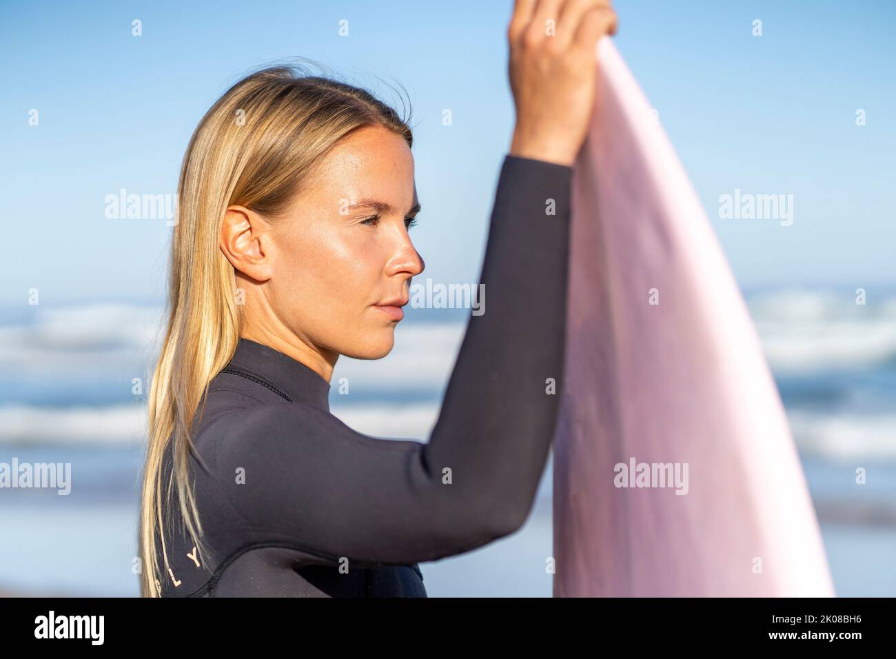 Surfer girl at the beach with her surfboard at sunrise looking at the waves in the morning. Female surfer woman Stock Photo