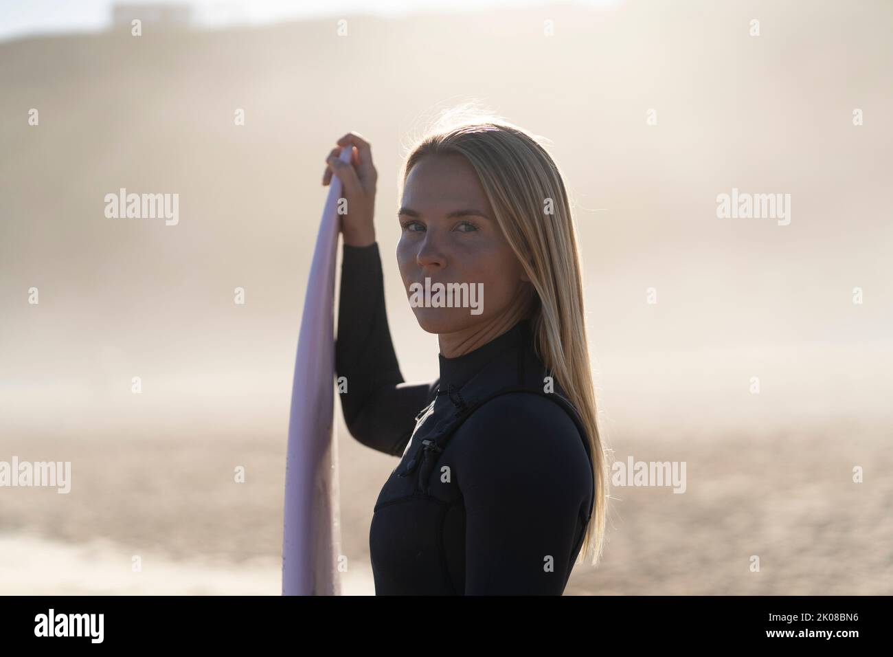 Surfer girl at the beach with her surfboard at sunrise looking at the waves. Female surfer woman Stock Photo